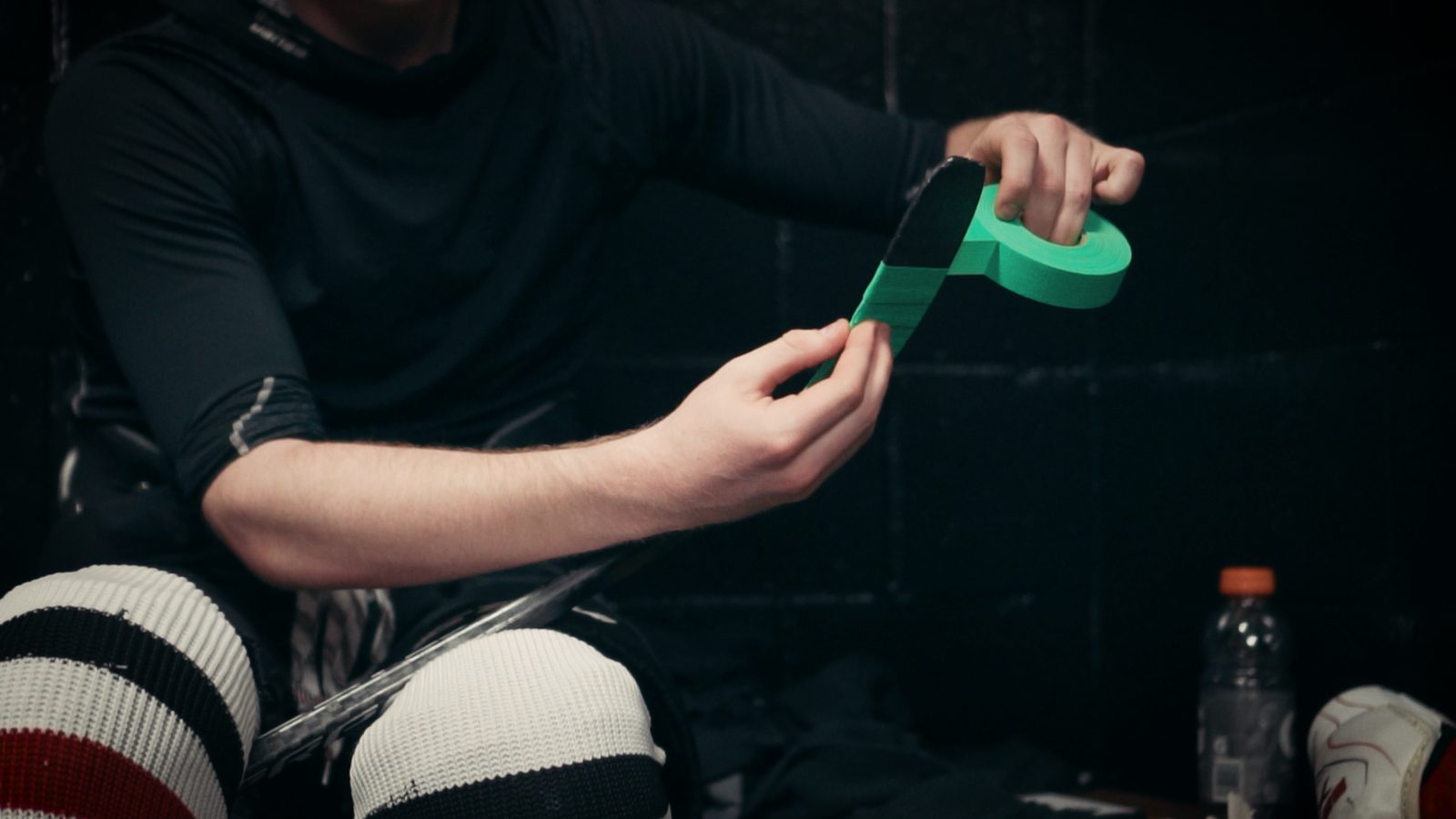 A player rolling green tape into a wristband in the locker room